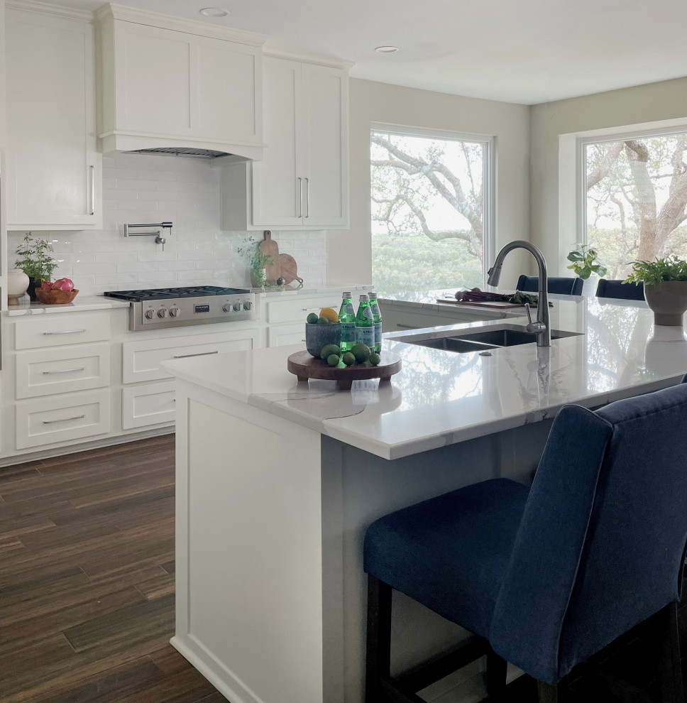 Example of a large ceramic tile and brown floor kitchen design with an undermount sink, shaker cabinets, white cabinets, white backsplash, subway tile backsplash, stainless steel appliances, an island and white countertops