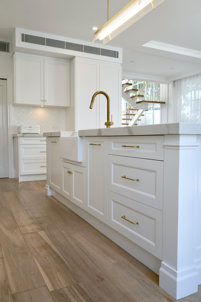 Idéer för att renovera ett stort vintage vit vitt kök, med en undermonterad diskho, luckor med infälld panel, vita skåp, bänkskiva i kvarts, vitt stänkskydd, stänkskydd i keramik, rostfria vitvaror, mellanmörkt trägolv, en köksö och brunt golv