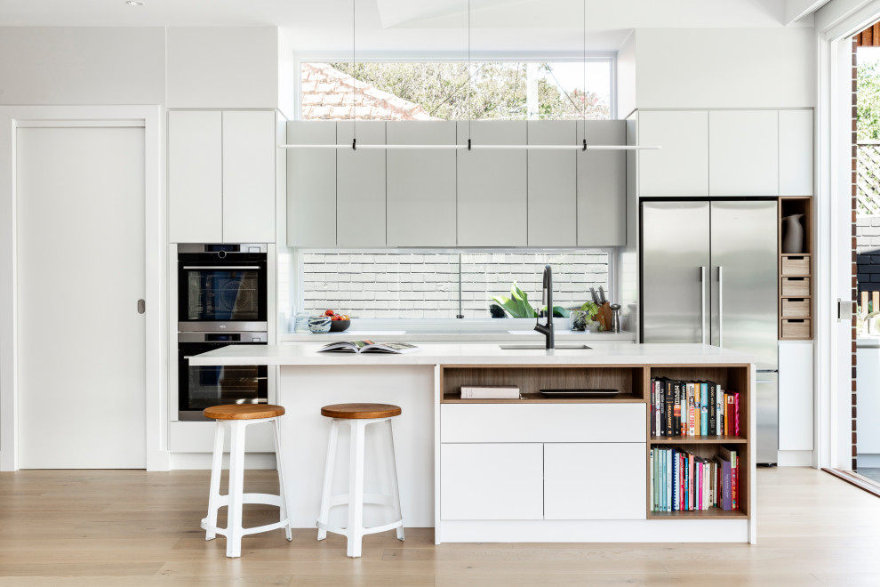 Beach style kitchen in Sydney with an undermount sink, flat-panel cabinets, grey cabinets, window splashback, stainless steel appliances, light hardwood floors, with island and white benchtop.