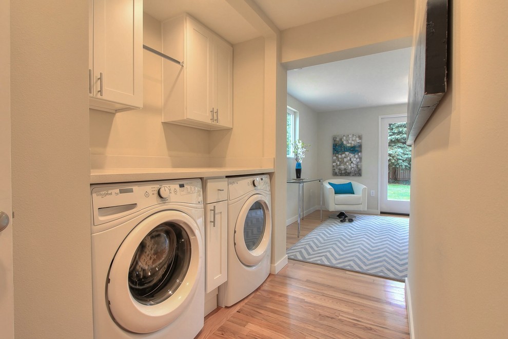 Inspiration for a small traditional galley laundry room in Seattle with shaker cabinets, white cabinets, beige walls, light hardwood floors and a side-by-side washer and dryer.