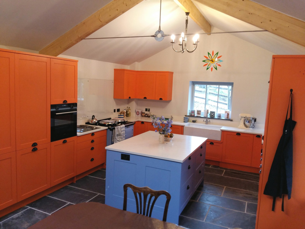 Inspiration for a large contemporary u-shaped open plan kitchen in Cornwall with a farmhouse sink, shaker cabinets, orange cabinets, quartz benchtops, white splashback, black appliances, slate floors, grey floor, white benchtop and exposed beam.