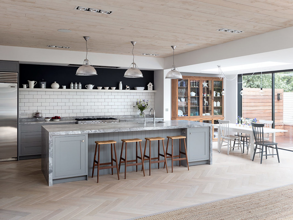 Design ideas for a large transitional galley open plan kitchen in London with an undermount sink, marble benchtops, white splashback, light hardwood floors, with island, beige floor, grey benchtop, shaker cabinets, grey cabinets, subway tile splashback and stainless steel appliances.