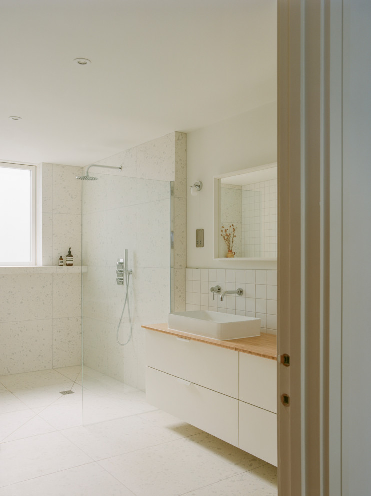 Design ideas for a large beach style ensuite wet room bathroom in Cornwall with open cabinets, white cabinets, a freestanding bath, a wall mounted toilet, white tiles, ceramic tiles, white walls, terrazzo flooring, a trough sink, wooden worktops, white floors, an open shower, double sinks and a built in vanity unit.