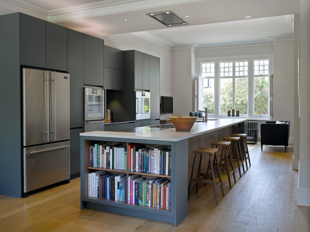 This is an example of a large transitional galley open plan kitchen in London with flat-panel cabinets, blue cabinets, solid surface benchtops, with island, stainless steel appliances and light hardwood floors.