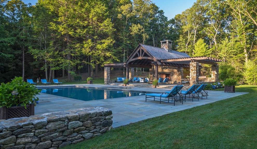 This is an example of a large country backyard rectangular natural pool in Boston with a pool house and concrete pavers.