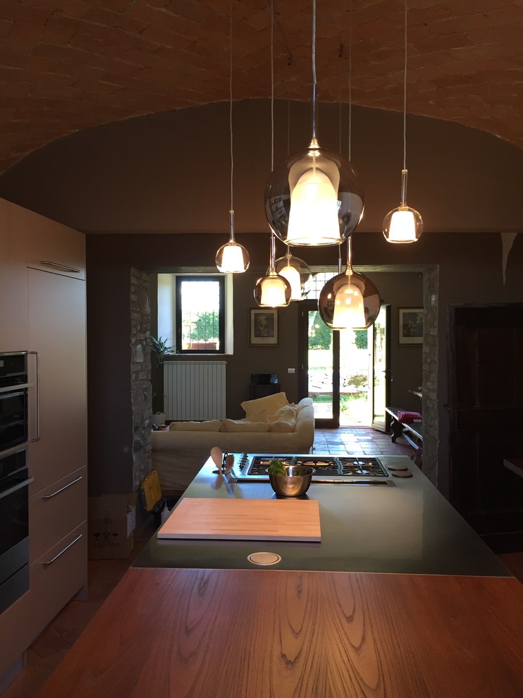 This is an example of a mid-sized country galley eat-in kitchen in Milan with flat-panel cabinets, grey cabinets, wood benchtops, brick floors, with island and brown floor.