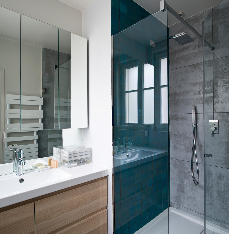 Photo of a contemporary 3/4 bathroom in Paris with flat-panel cabinets, light wood cabinets, a corner shower, blue tile, gray tile, green tile, white walls, an integrated sink and a hinged shower door.