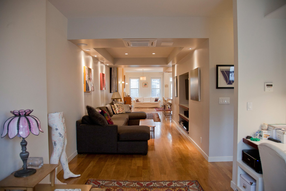 This is an example of a mid-sized traditional open concept living room in New York with white walls, light hardwood floors and a built-in media wall.