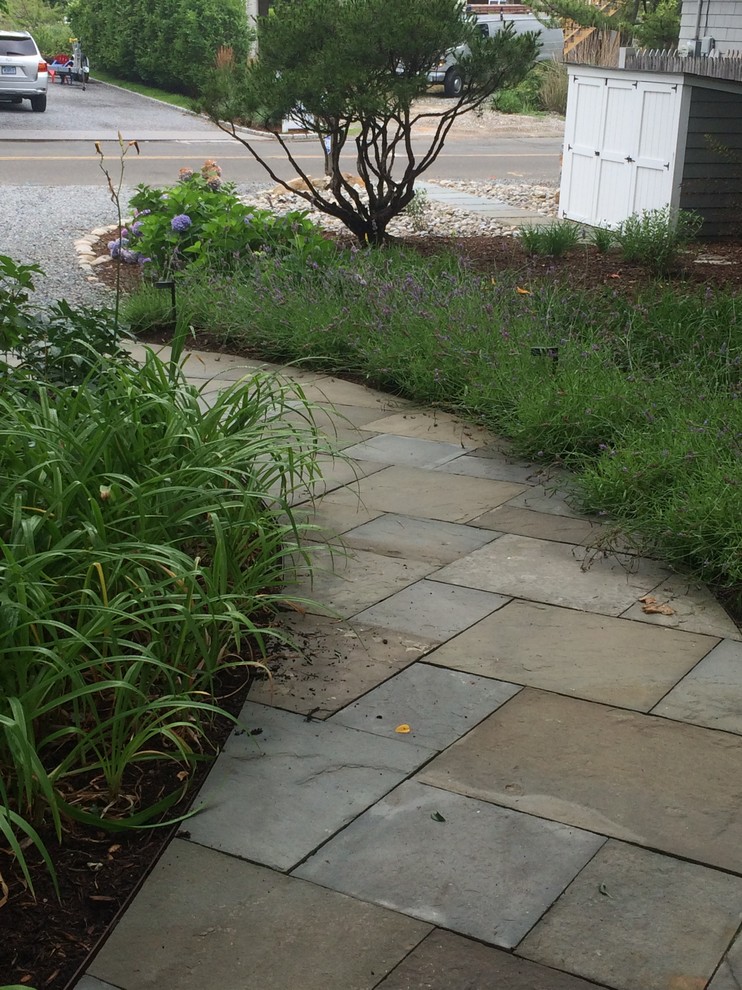 This is an example of a small beach style front yard shaded driveway in New York with a garden path and natural stone pavers.