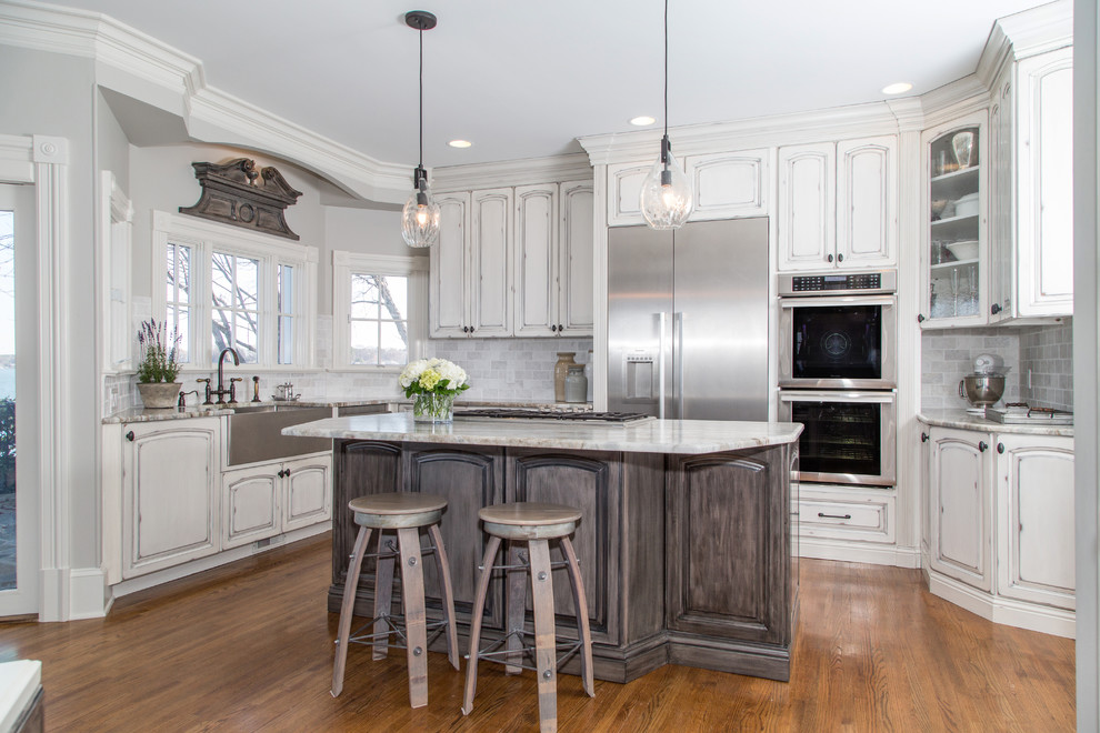 Design ideas for a mid-sized transitional u-shaped eat-in kitchen in Charlotte with a farmhouse sink, raised-panel cabinets, distressed cabinets, quartzite benchtops, white splashback, marble splashback, stainless steel appliances, medium hardwood floors, with island and brown floor.