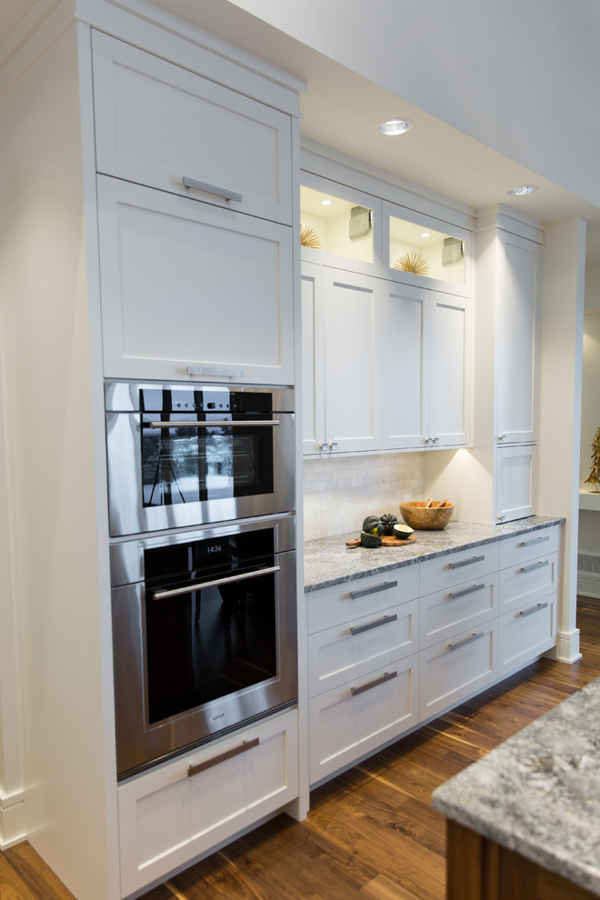 Inspiration for a mid-sized transitional l-shaped medium tone wood floor eat-in kitchen remodel in Vancouver with an undermount sink, shaker cabinets, white cabinets, granite countertops, white backsplash, white appliances and an island