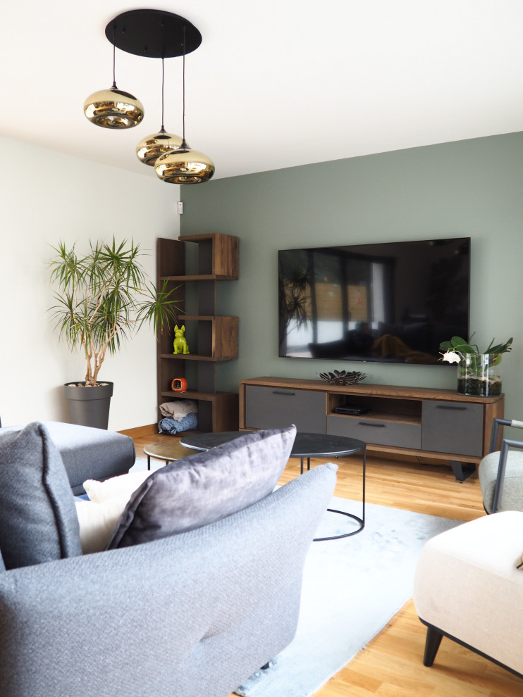 Réalisation d'un très grand salon design avec un mur vert, parquet clair et un téléviseur fixé au mur.