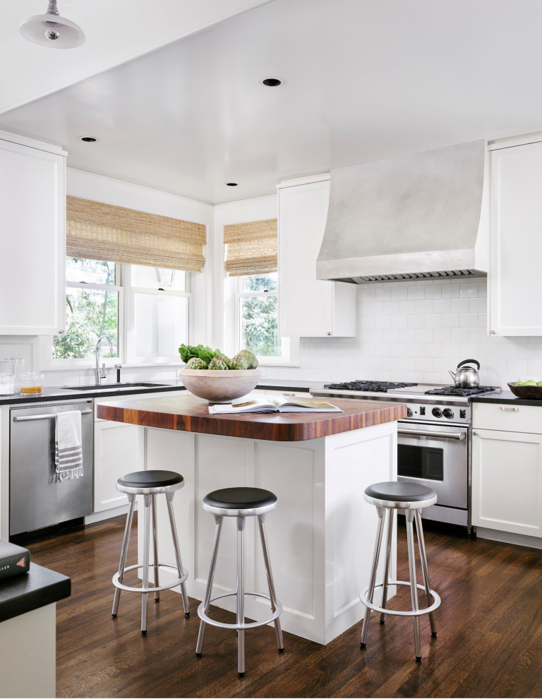 Inspiration for a mid-sized transitional l-shaped kitchen in Austin with recessed-panel cabinets, white cabinets, white splashback, ceramic splashback, stainless steel appliances, dark hardwood floors, with island, brown floor, black benchtop and an undermount sink.