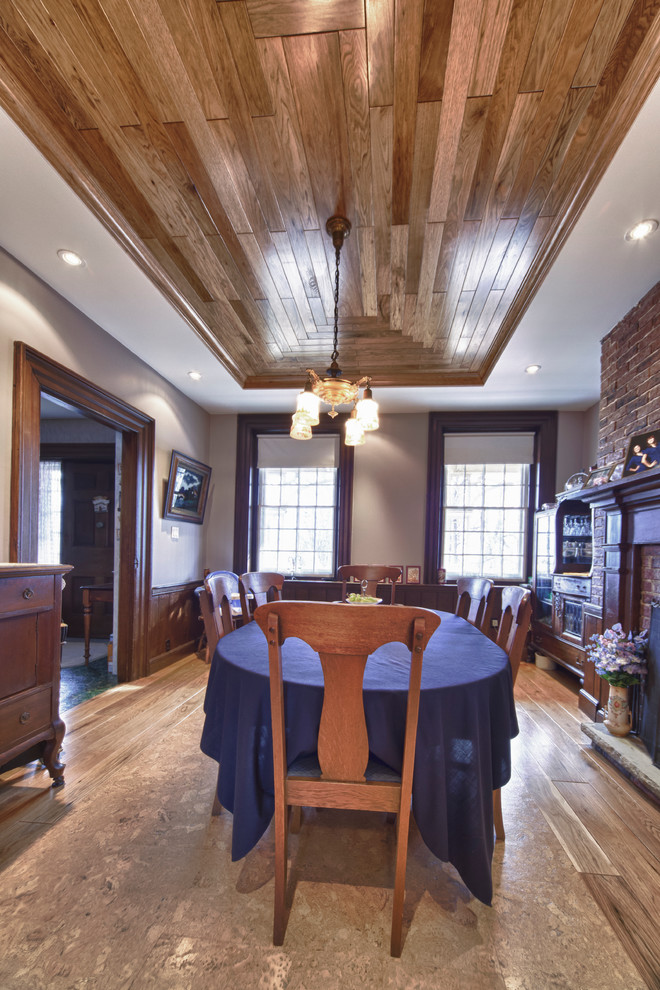 This is an example of a large country separate dining room in Toronto with grey walls, plywood floors, a standard fireplace and a wood fireplace surround.