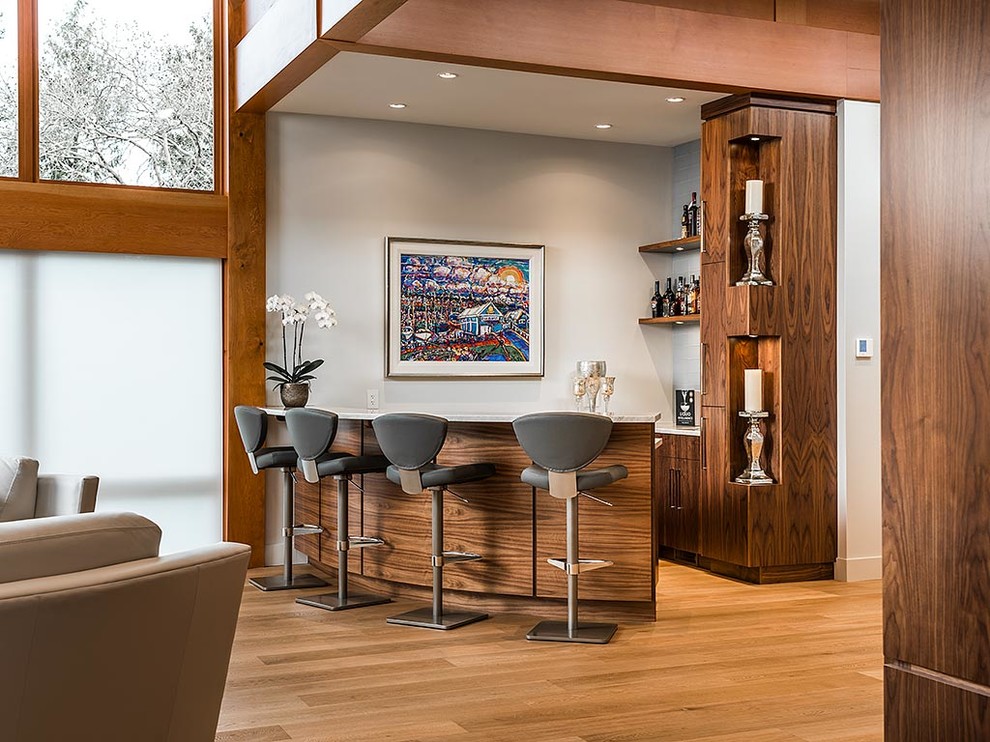 Photo of a mid-sized contemporary u-shaped seated home bar in Vancouver with flat-panel cabinets, grey splashback, brown floor, dark wood cabinets and medium hardwood floors.