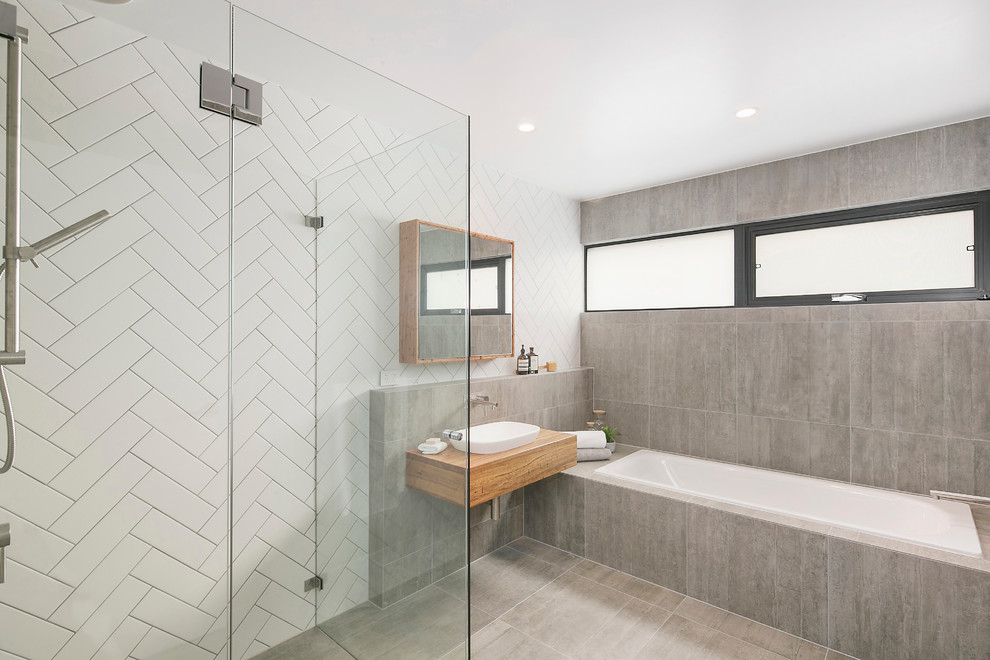 This is an example of a contemporary bathroom in Sydney with a drop-in tub, a curbless shower, gray tile, a vessel sink and wood benchtops.
