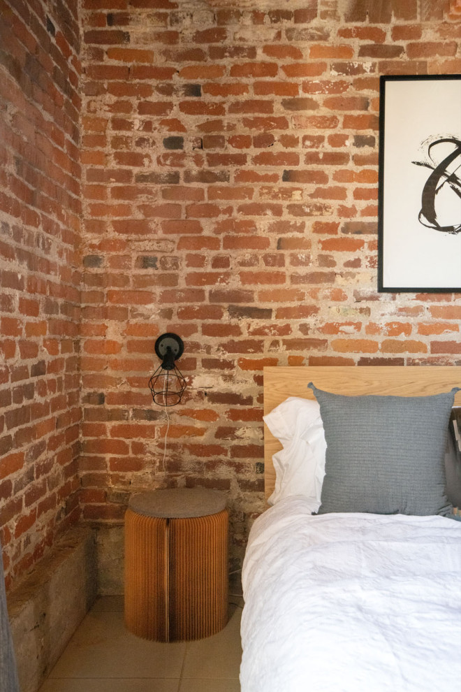 This is an example of an industrial mezzanine bedroom in Sacramento with porcelain flooring, beige floors, exposed beams and brick walls.