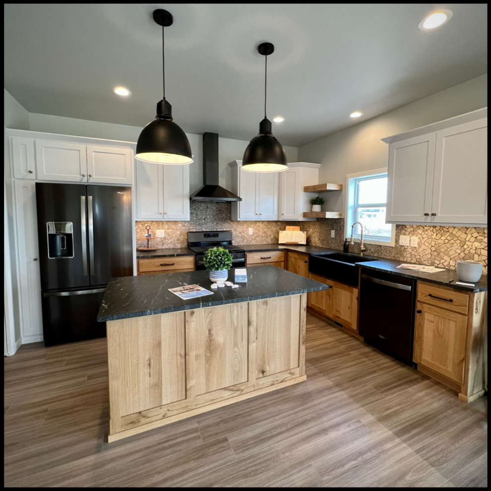 Example of a mountain style kitchen design with white cabinets, black appliances, an island and black countertops