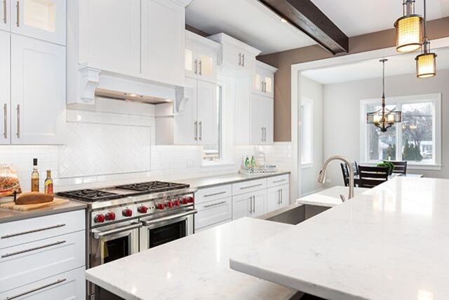 Open concept kitchen - transitional u-shaped dark wood floor open concept kitchen idea in Chicago with a farmhouse sink, shaker cabinets, white cabinets, quartz countertops, white backsplash, subway tile backsplash, stainless steel appliances, an island and white countertops