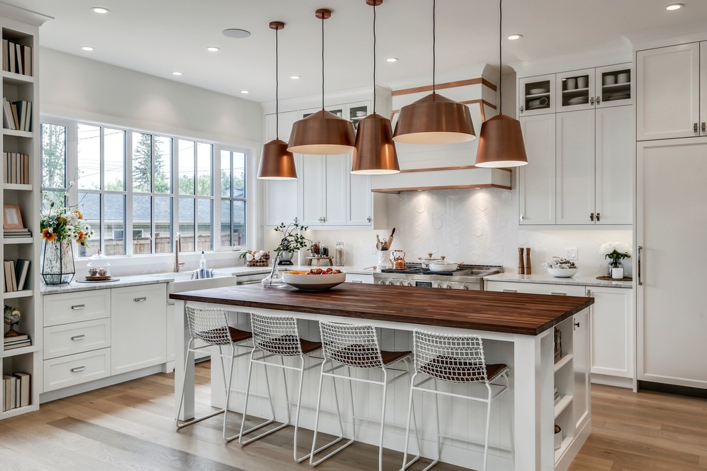 Inspiration for a large country u-shaped eat-in kitchen in Calgary with a farmhouse sink, shaker cabinets, white cabinets, wood benchtops, ceramic splashback, panelled appliances, light hardwood floors, with island, beige floor and white splashback.
