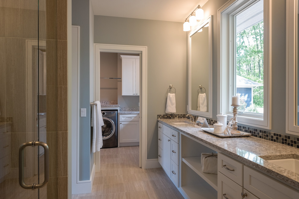 This is an example of a large arts and crafts master bathroom in Grand Rapids with recessed-panel cabinets, white cabinets, an alcove shower, brown tile, porcelain tile, grey walls, porcelain floors, an undermount sink, granite benchtops, beige floor, a hinged shower door and a laundry.