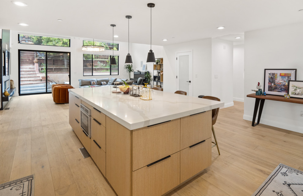 Inspiration for a large modern kitchen/diner in San Francisco with a built-in sink, flat-panel cabinets, light wood cabinets, grey splashback, glass tiled splashback, stainless steel appliances, light hardwood flooring, an island, yellow floors and white worktops.