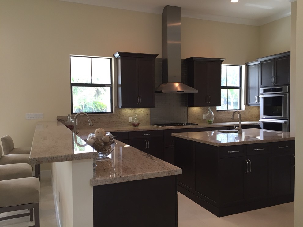 Large contemporary u-shaped open plan kitchen in Miami with a drop-in sink, recessed-panel cabinets, dark wood cabinets, granite benchtops, grey splashback, stainless steel appliances, travertine floors and with island.
