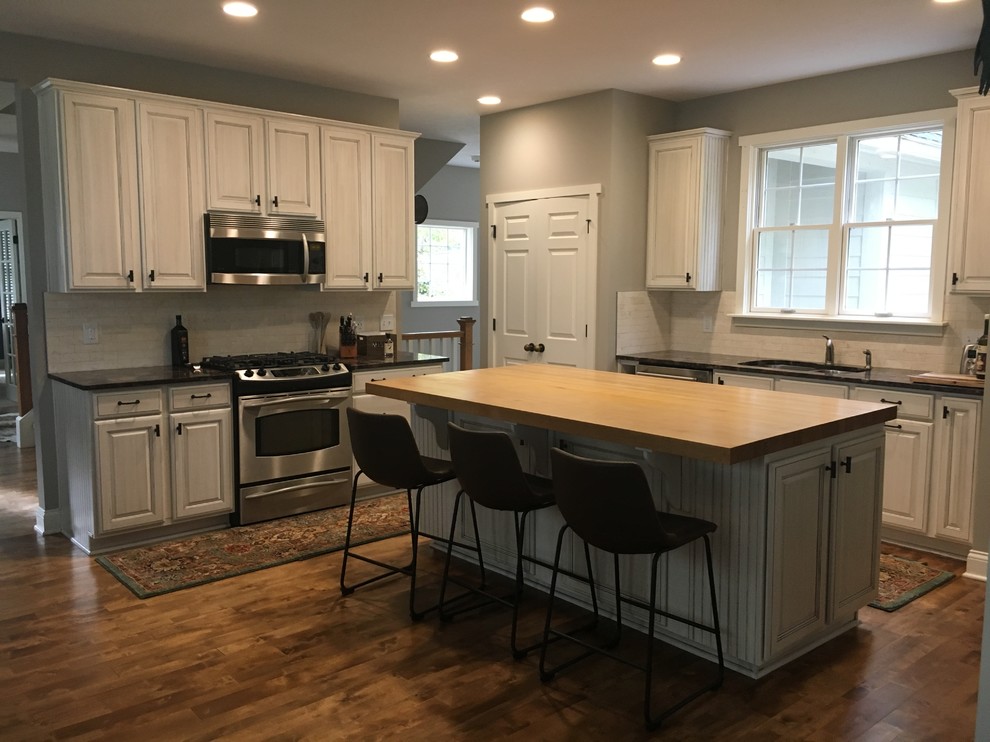 Mid-sized mountain style l-shaped light wood floor and brown floor eat-in kitchen photo in Indianapolis with an undermount sink, shaker cabinets, white cabinets, quartzite countertops, gray backsplash, travertine backsplash, stainless steel appliances, an island and black countertops