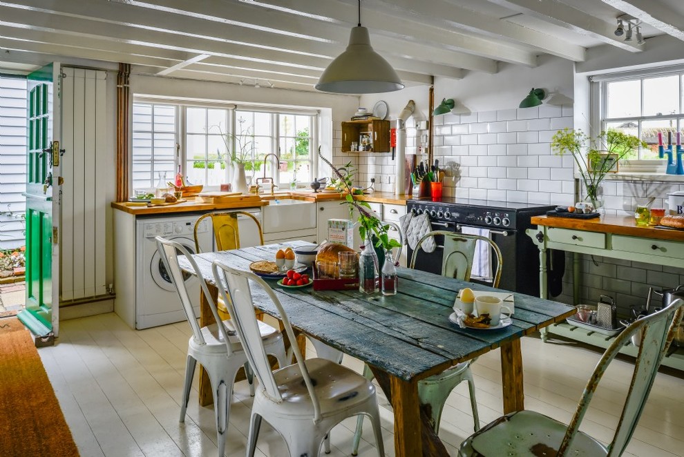 Design ideas for a mid-sized eclectic u-shaped eat-in kitchen in Cornwall with a farmhouse sink, shaker cabinets, green cabinets, wood benchtops, white splashback, ceramic splashback, black appliances, painted wood floors and white floor.