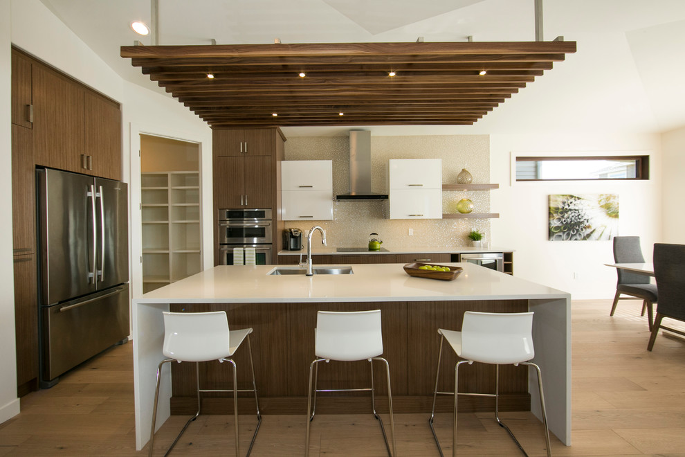 Design ideas for a mid-sized contemporary l-shaped eat-in kitchen in Edmonton with a double-bowl sink, flat-panel cabinets, medium wood cabinets, quartz benchtops, metallic splashback, glass tile splashback, stainless steel appliances, light hardwood floors and with island.