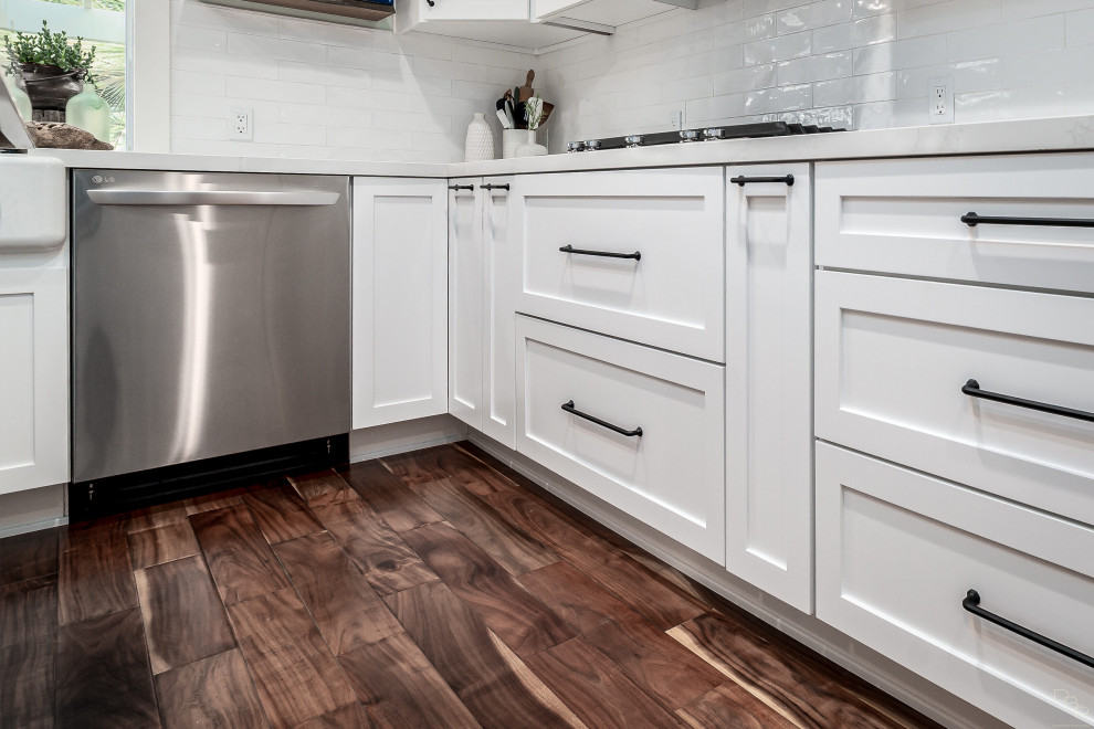Photo of a medium sized country u-shaped kitchen/diner in San Diego with a belfast sink, shaker cabinets, white cabinets, composite countertops, white splashback, ceramic splashback, stainless steel appliances, vinyl flooring, an island and multicoloured worktops.
