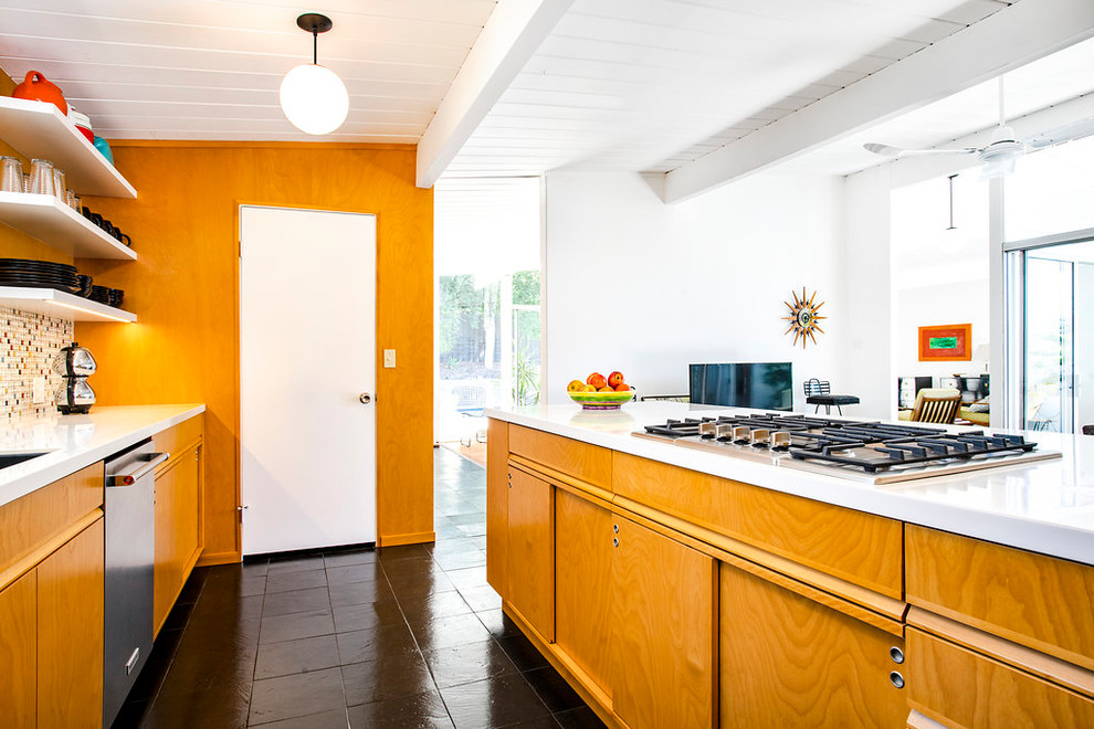 Design ideas for a mid-sized midcentury galley open plan kitchen in Los Angeles with an undermount sink, flat-panel cabinets, multi-coloured splashback, stainless steel appliances, a peninsula, black floor, white benchtop, medium wood cabinets, solid surface benchtops, mosaic tile splashback and slate floors.