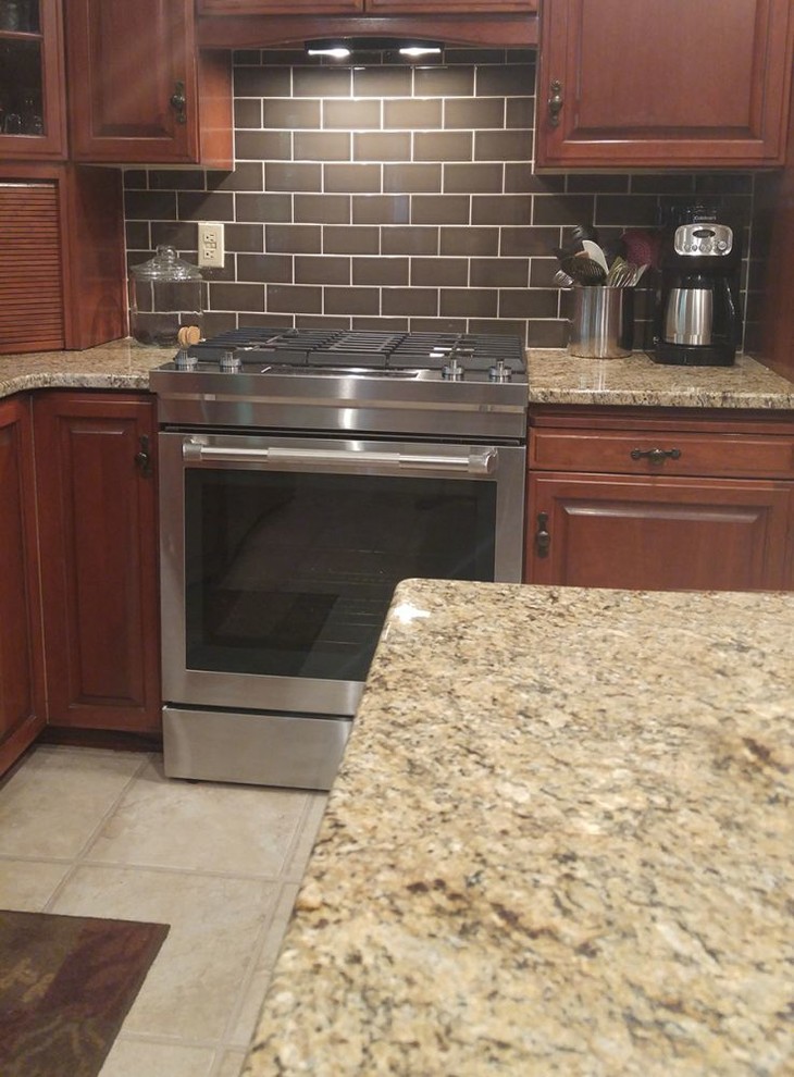 Kitchen - mid-sized transitional l-shaped ceramic tile kitchen idea with raised-panel cabinets, dark wood cabinets, granite countertops, brown backsplash, subway tile backsplash, stainless steel appliances and an island