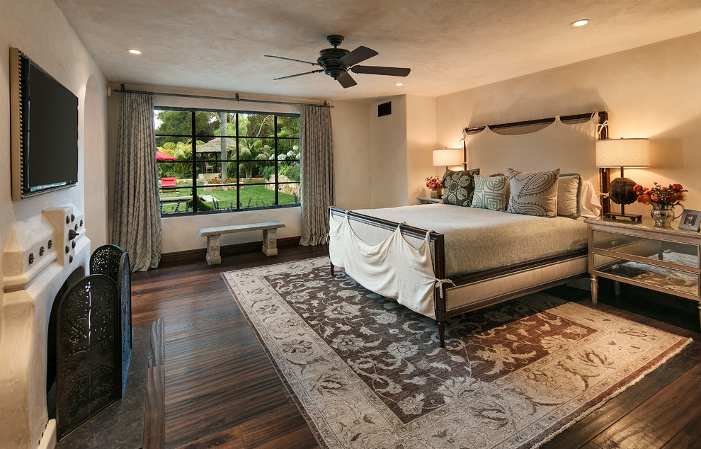 Large mediterranean guest bedroom in Santa Barbara with beige walls, dark hardwood floors, a standard fireplace and a plaster fireplace surround.