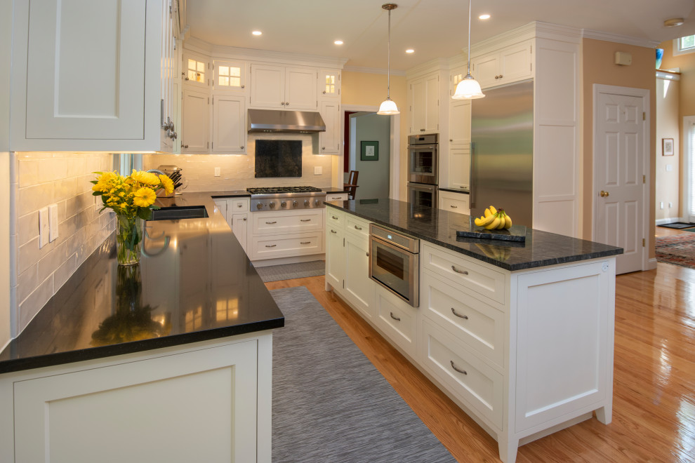 Example of a mid-sized minimalist medium tone wood floor and brown floor eat-in kitchen design in Boston with an undermount sink, shaker cabinets, white cabinets, quartzite countertops, white backsplash, ceramic backsplash, stainless steel appliances, an island and black countertops