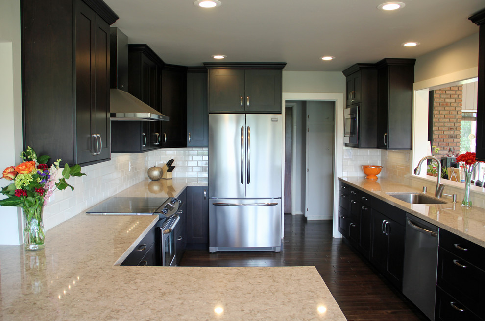 Example of a mid-sized transitional u-shaped dark wood floor and brown floor kitchen design in Sacramento with an undermount sink, shaker cabinets, dark wood cabinets, solid surface countertops, white backsplash, subway tile backsplash, stainless steel appliances, gray walls and a peninsula