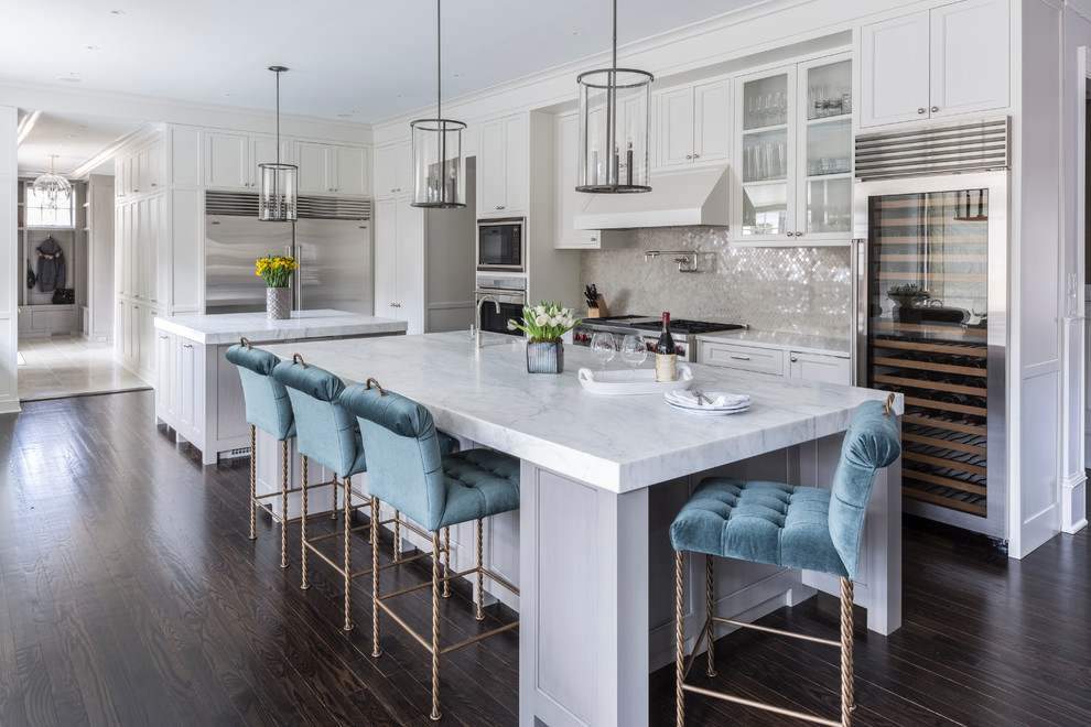 Design ideas for an expansive transitional eat-in kitchen in New York with an undermount sink, raised-panel cabinets, white cabinets, marble benchtops, white splashback, mosaic tile splashback, stainless steel appliances, dark hardwood floors and multiple islands.