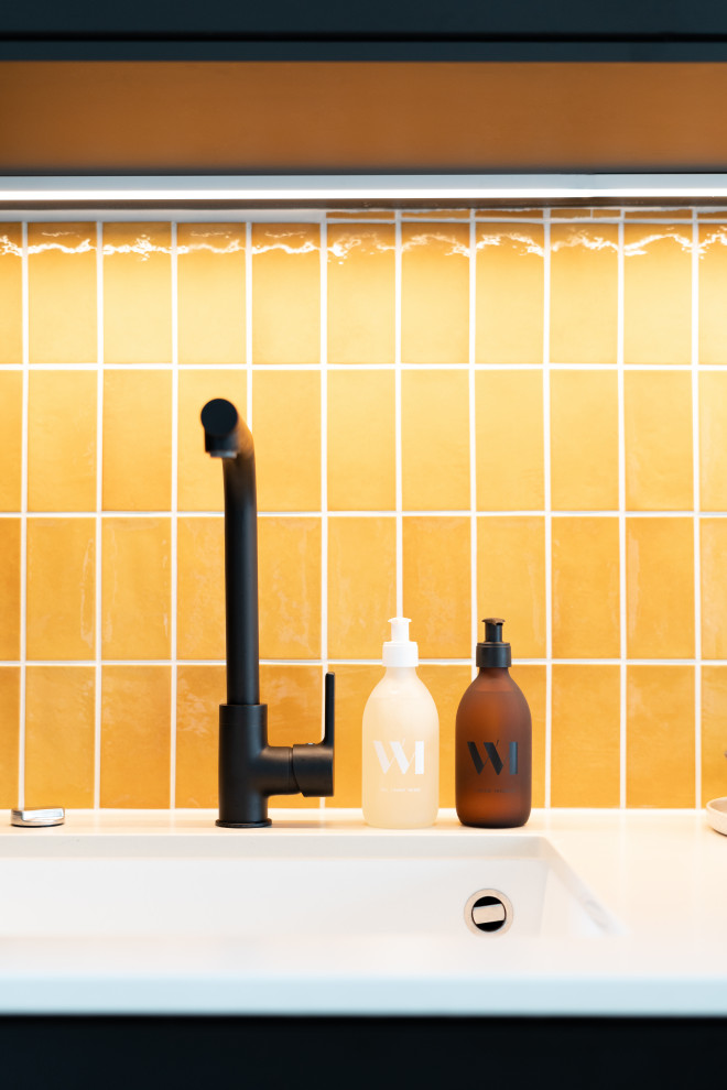 Idee per una grande cucina minimalista con lavello sottopiano, ante nere, top in quarzite, paraspruzzi giallo, elettrodomestici da incasso, pavimento in legno massello medio, pavimento marrone e top bianco