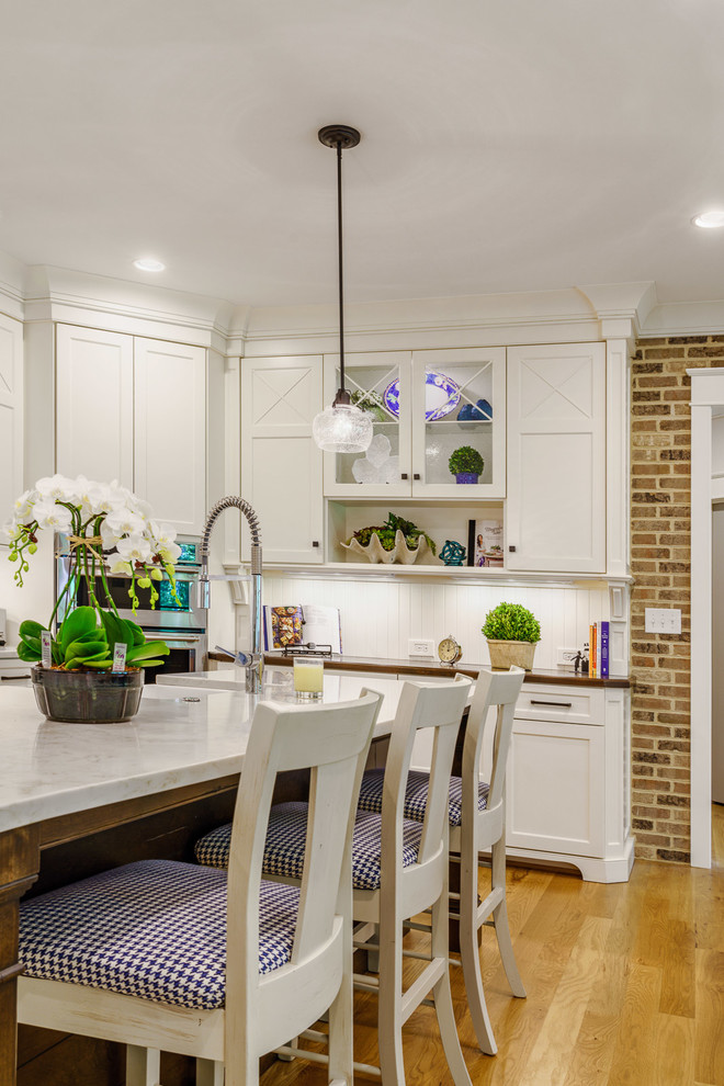 Eat-in kitchen - large transitional u-shaped medium tone wood floor and brown floor eat-in kitchen idea with a farmhouse sink, recessed-panel cabinets, white cabinets, quartz countertops, white backsplash, ceramic backsplash, stainless steel appliances, an island and white countertops