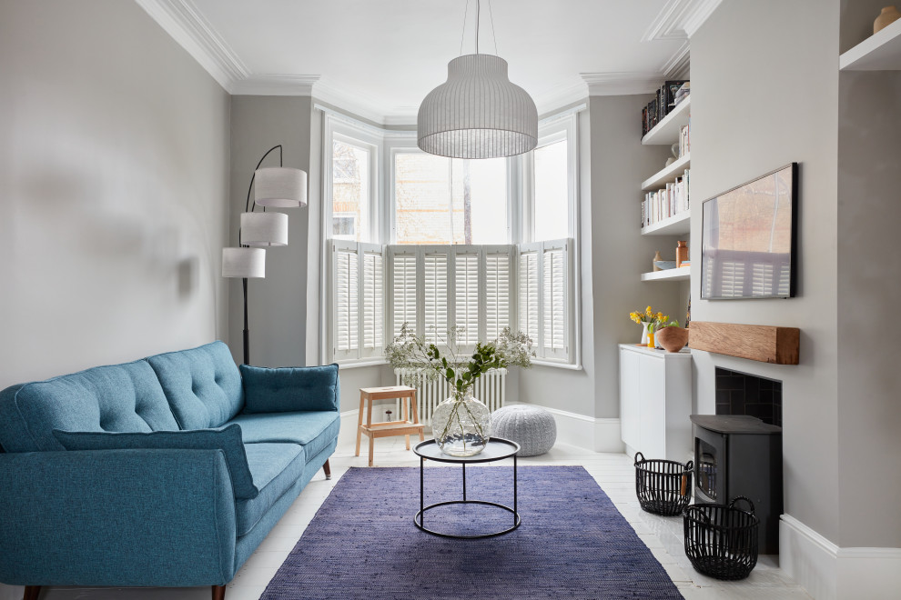 Skandinavisches Wohnzimmer mit grauer Wandfarbe, gebeiztem Holzboden, Kamin, TV-Wand und weißem Boden in London