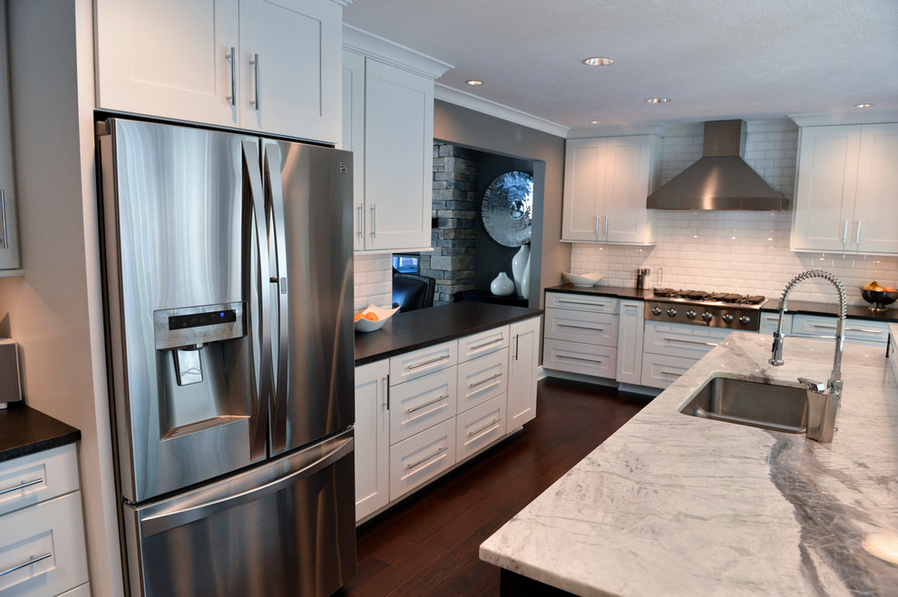 Inspiration for a transitional dark wood floor kitchen remodel in Cleveland with a drop-in sink, recessed-panel cabinets, white backsplash, ceramic backsplash, stainless steel appliances and an island