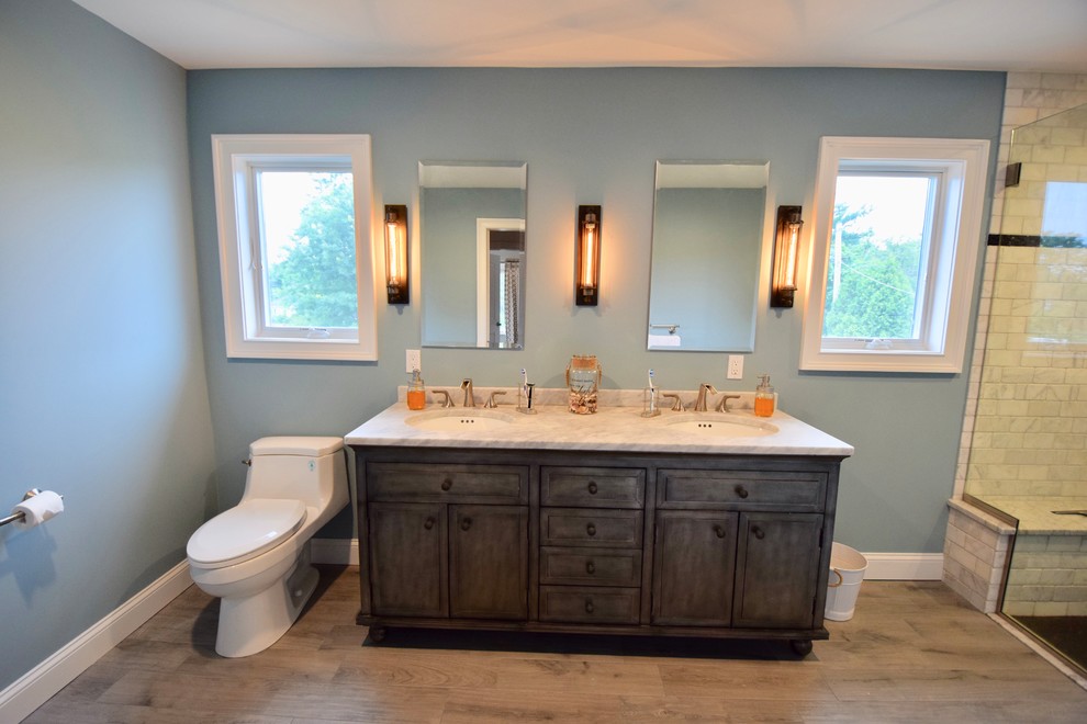 Example of a large transitional master gray tile and marble tile porcelain tile and brown floor doorless shower design with recessed-panel cabinets, dark wood cabinets, a one-piece toilet, blue walls, an undermount sink, marble countertops, a hinged shower door and gray countertops