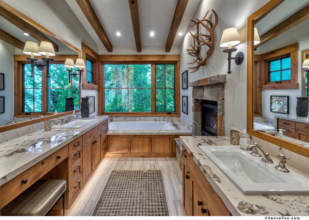 This is an example of a contemporary master bathroom in Other with shaker cabinets, light wood cabinets, a drop-in tub, beige tile, stone slab, beige walls, porcelain floors, a drop-in sink, granite benchtops, grey floor, white benchtops, a double vanity, a built-in vanity and exposed beam.