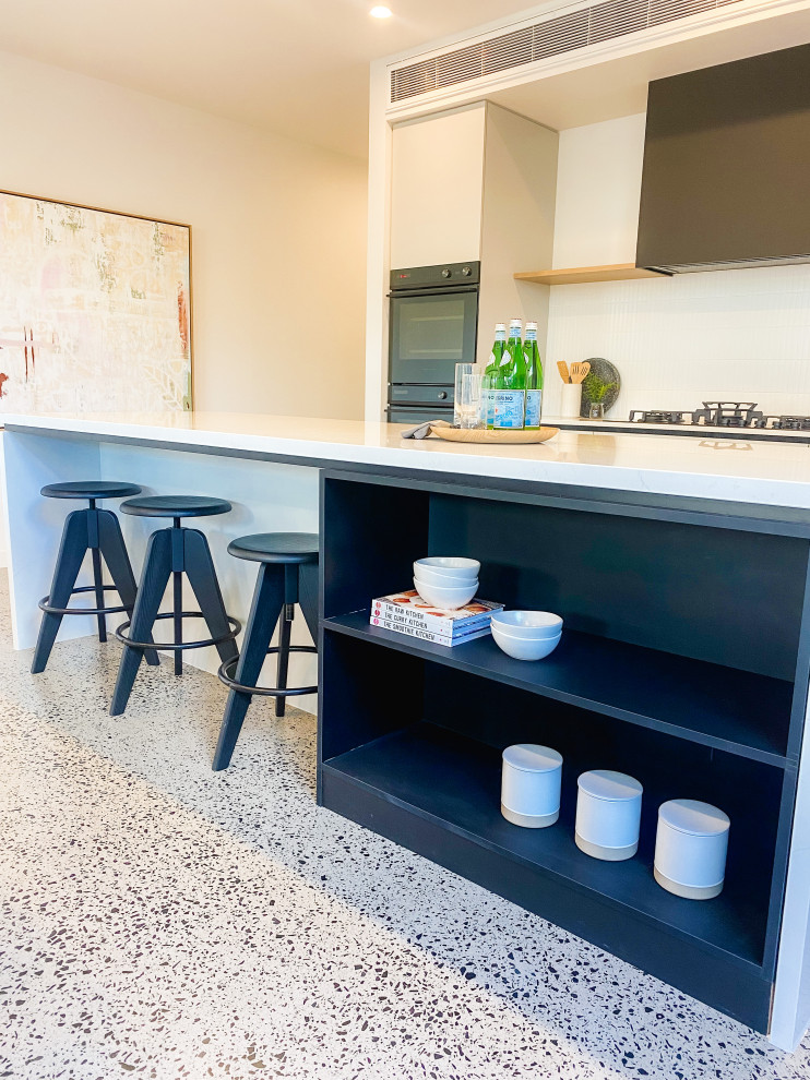 Inspiration for a large contemporary l-shaped open plan kitchen in Melbourne with a double-bowl sink, beaded inset cabinets, grey cabinets, quartz benchtops, white splashback, ceramic splashback, black appliances, concrete floors, with island, grey floor and white benchtop.