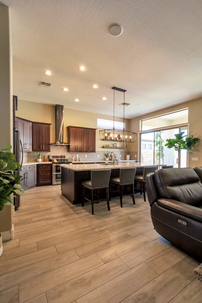 Mid-sized transitional l-shaped porcelain tile and brown floor open concept kitchen photo in Phoenix with a single-bowl sink, shaker cabinets, brown cabinets, granite countertops, gray backsplash, brick backsplash, stainless steel appliances, an island and multicolored countertops