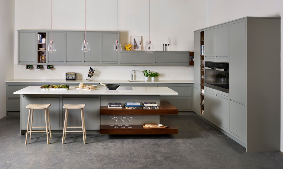 Inspiration for a contemporary l-shaped kitchen in London with flat-panel cabinets, grey cabinets, black appliances, concrete floors, with island, grey floor and white benchtop.