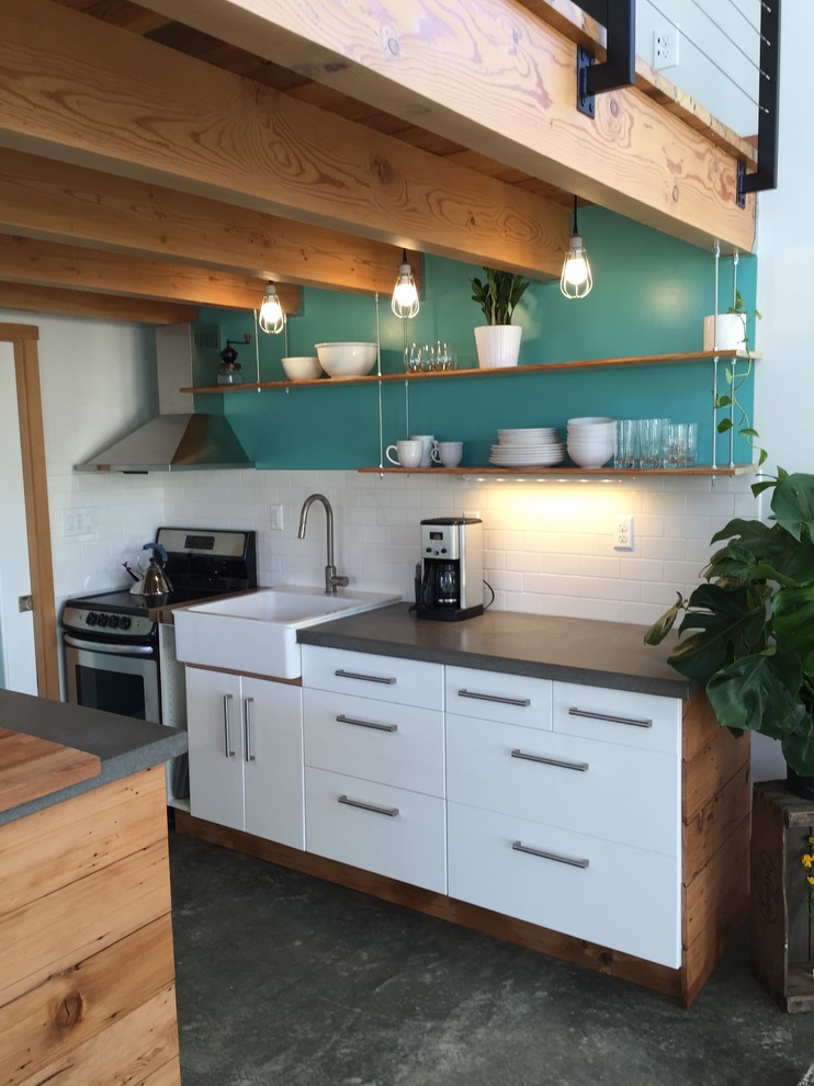 This is an example of a small modern galley open plan kitchen in Portland with a farmhouse sink, flat-panel cabinets, white cabinets, concrete benchtops, white splashback, ceramic splashback, stainless steel appliances, concrete floors, with island and grey floor.
