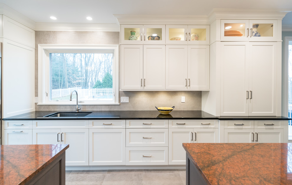 Photo of a large transitional galley open plan kitchen in Bridgeport with an undermount sink, recessed-panel cabinets, white cabinets, granite benchtops, grey splashback, ceramic splashback, stainless steel appliances, ceramic floors, multiple islands, grey floor and black benchtop.