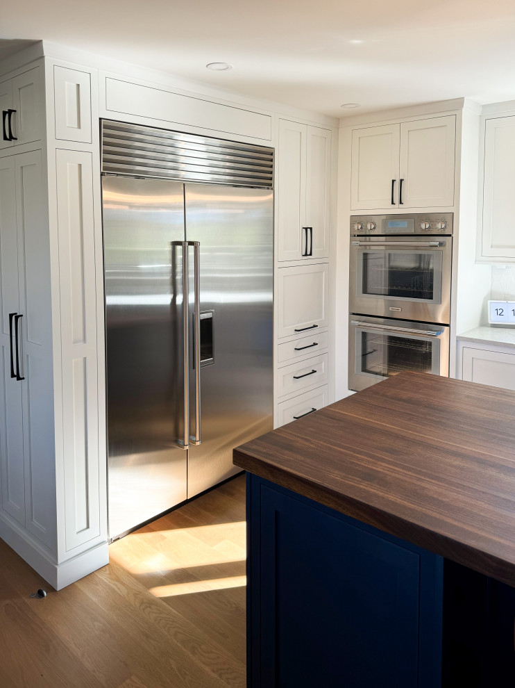 Example of a mid-sized transitional l-shaped medium tone wood floor and brown floor eat-in kitchen design with an undermount sink, shaker cabinets, white cabinets, white backsplash, stainless steel appliances, an island and white countertops