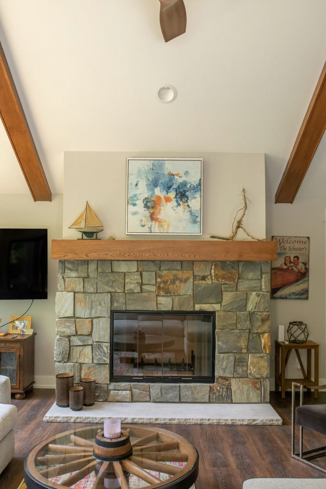 Cette image montre une salle de séjour ouverte avec un mur gris, un sol en vinyl, une cheminée standard, un manteau de cheminée en pierre, un téléviseur d'angle, un sol marron et un plafond voûté.
